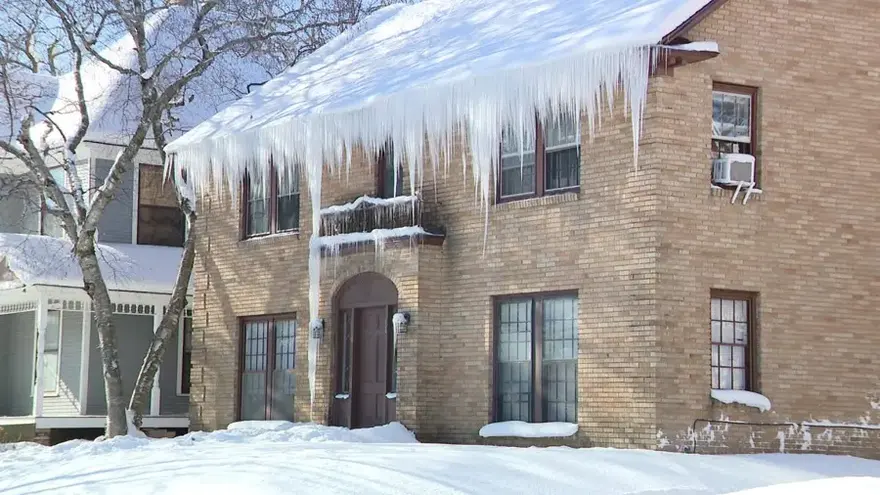 Heavy icicles and an ice dam along the eaves of a brick colonial
